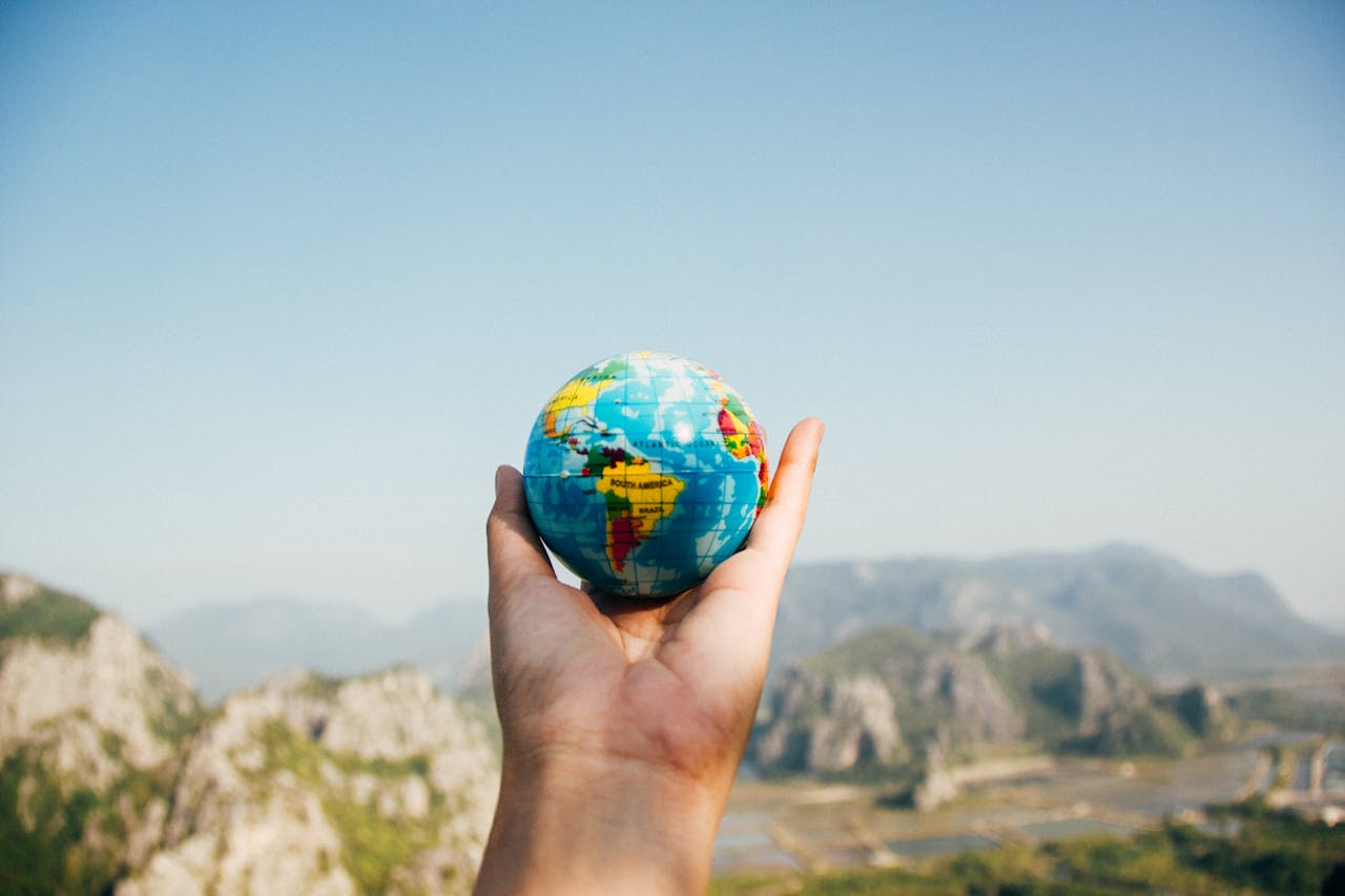 stats-img Hand holding a globe against a mountain background symbolizing travel and exploration.
