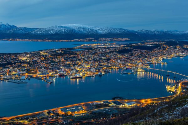 Stunning aerial view of Tromsø at night. Illuminated cityscape with harbor and mountains, captured in vibrant colors.
